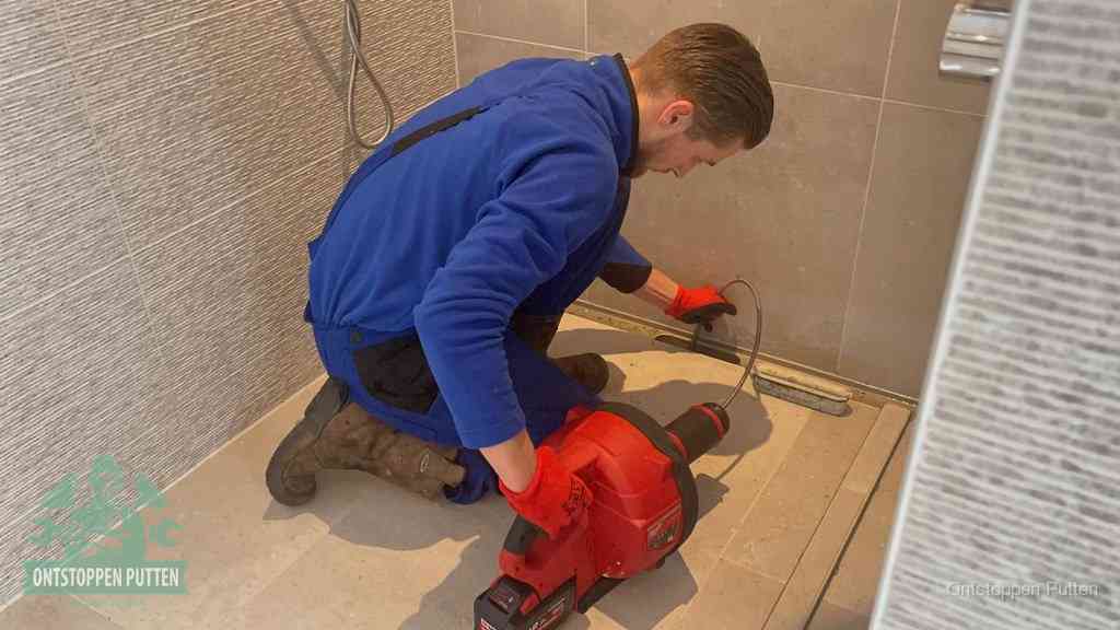 Een monteur ontstopt een langwerpige douchegoot met een elektrische veer, een doucheputje verstopt door haren en zeep in Putten