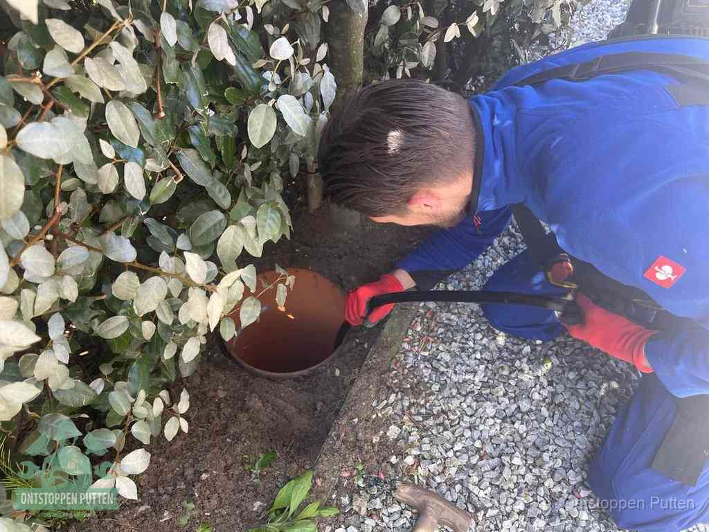 Een monteur voert een slang in een geopende rioolput in de tuin om het hoofdriool te ontstoppen in Putten